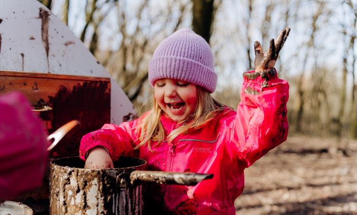 A child laughs as they play in the mud kitchen at WWT Llanelli